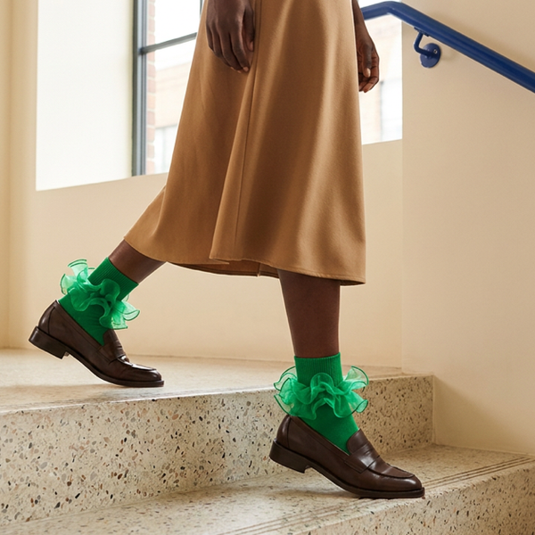Emerald ruffle ankle socks with brown loafers and a camel midi skirt on indoor steps.