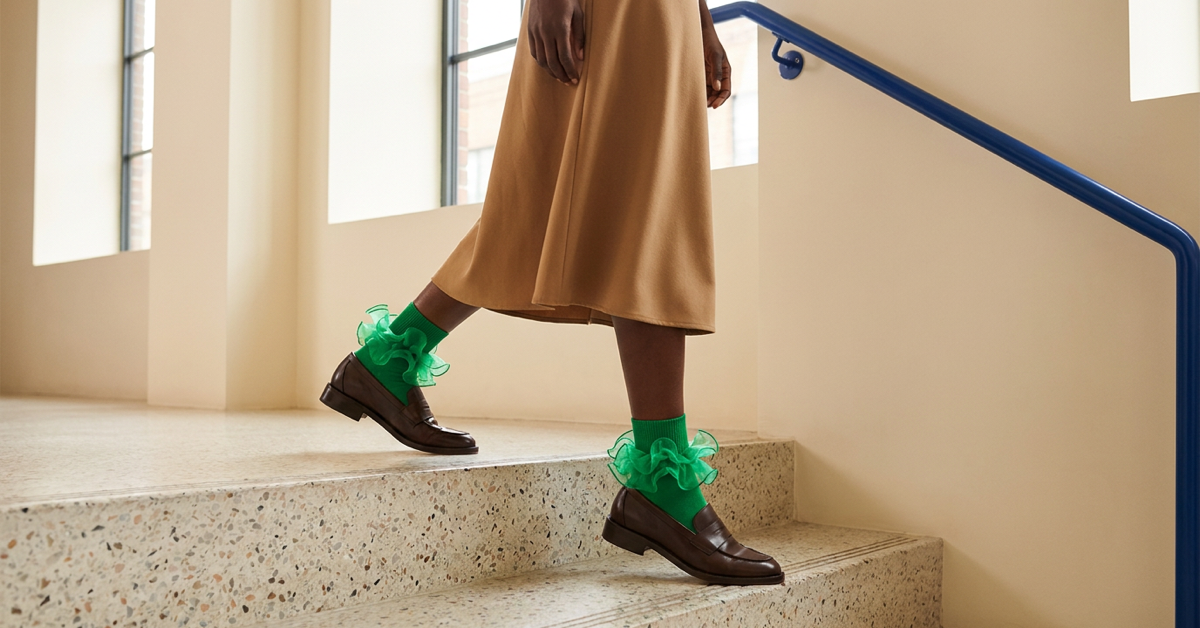 Emerald ruffle ankle socks with brown loafers and a camel midi skirt on indoor steps.