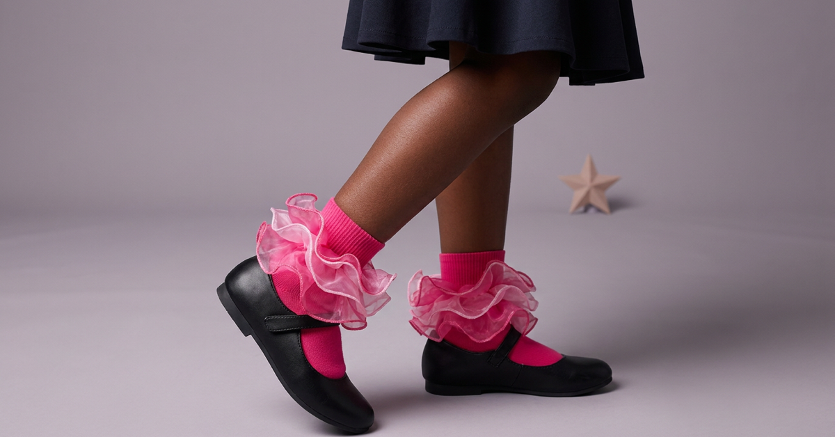 A girl wearing hot-pink layered ruffle socks with black Mary Jane shoes in a softly lit studio.