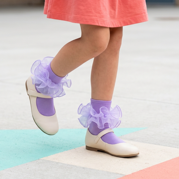 A girl wearing purple fold-cuff ruffle socks with cream Mary Jane shoes while stepping across a colorful floor.