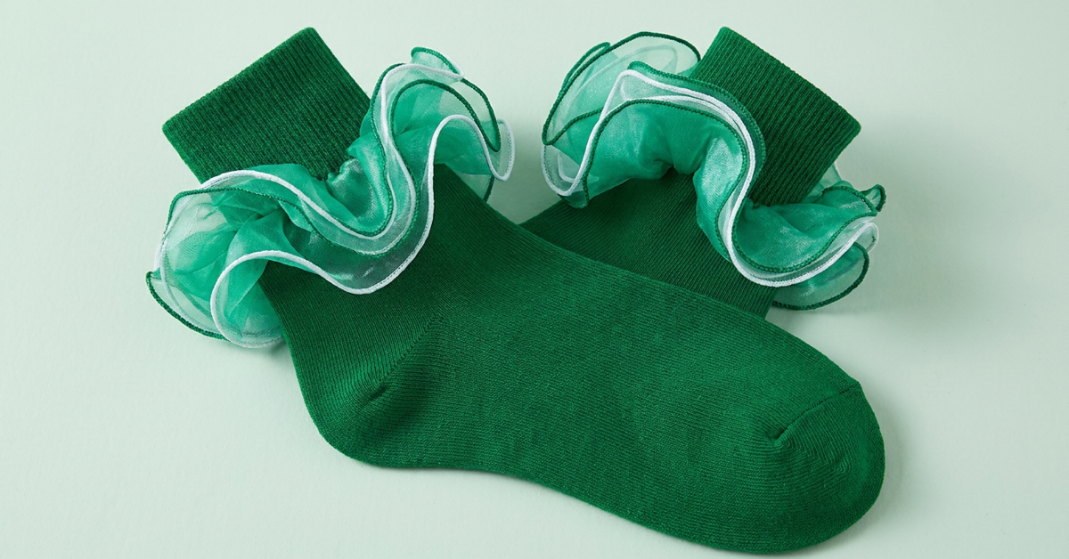 A pair of emerald green ankle socks with layered sheer ruffles shown close up on a pale mint surface.