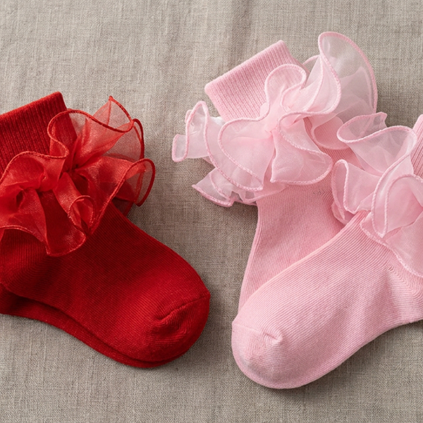 Red and pale pink girls' ruffle socks arranged as two pairs on natural linen.