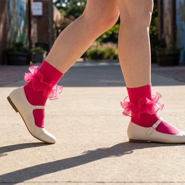 Hot pink ruffle ankle socks worn with cream Mary Jane flats, with the shoe straps and ruffle cuffs visible.