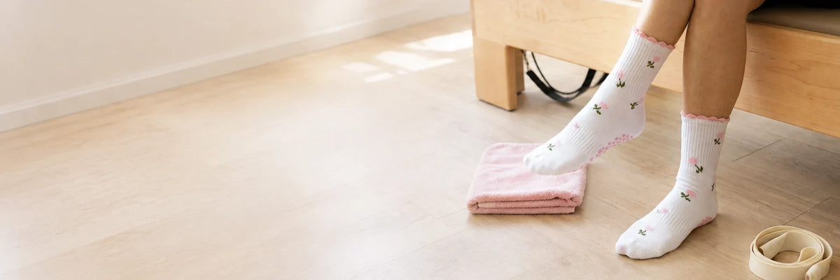 Woman wearing white floral grip socks beside a Pilates reformer